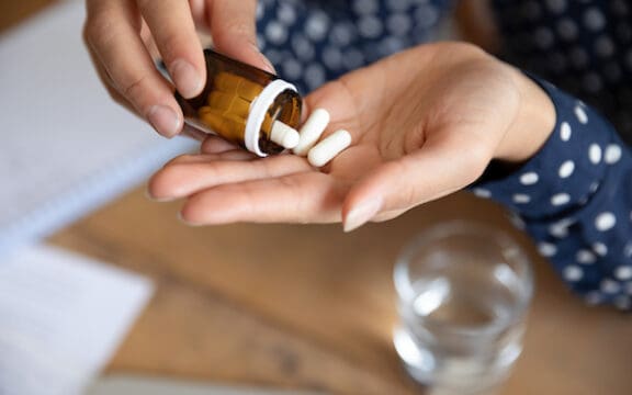 The question who takes antidepressants represented by hands pouring pills out of a bottle