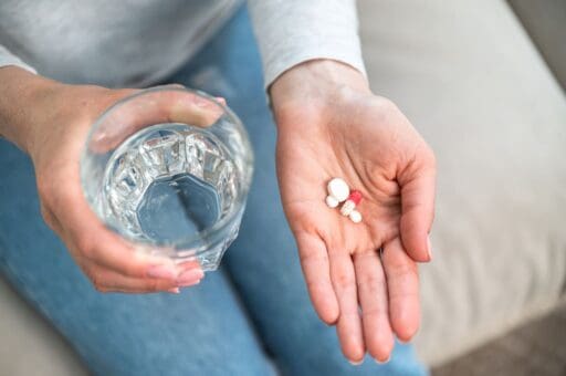 A hand holding a glass of water and medication pills in palm without knowing the paradoxical effect of antidepressants