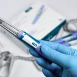 Hands in blue surgical gloves holding Ozempic Insulin injection pen, usually for diabetics but new research suggests we may use Ozempic for mental health