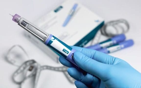 Hands in blue surgical gloves holding Ozempic Insulin injection pen, usually for diabetics but new research suggests we may use Ozempic for mental health