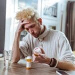 A person sitting and holding their head in their hands while looking at the pill bottles, unsure what to do when antidepressants stop working