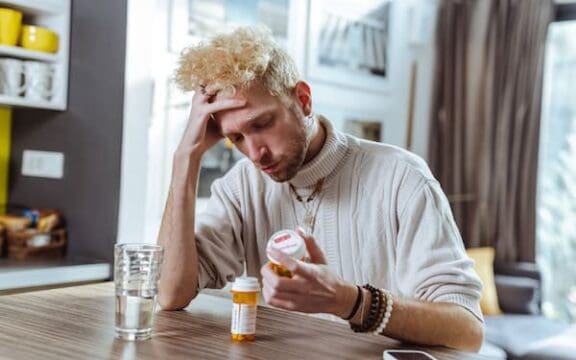 A person sitting and holding their head in their hands while looking at the pill bottles, unsure what to do when antidepressants stop working
